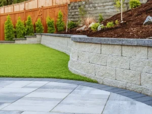 Curved retaining wall, artificial turf and light-coloured paver patio.