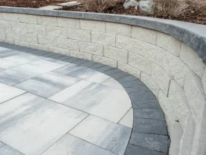 Curved light-coloured paver patio beside a low retaining wall.