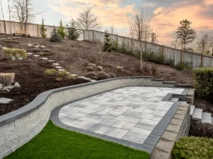 Completed paver patio and landscaped retaining wall on a sloping backyard.
